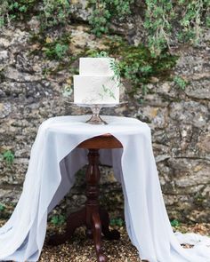 a white wedding cake sitting on top of a wooden table next to a stone wall