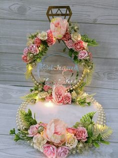 two cakes decorated with flowers and greenery on top of each other in front of a wooden wall