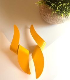 two pieces of yellow plastic sitting next to a potted plant on a white surface