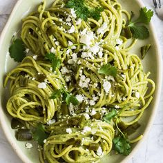 a bowl filled with green pasta and topped with fettuccine, parmesan cheese and cilantro