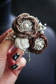 a hand holding a flower brooch with pearls on it's center and flowers in the middle