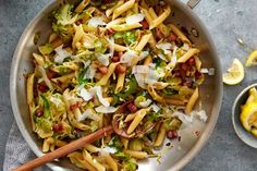 a pan filled with pasta and vegetables on top of a table next to lemon wedges