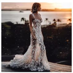 a woman in a white dress standing on a wooden deck near the water at sunset