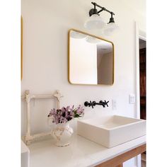 a white sink sitting under a bathroom mirror next to a vase with flowers in it