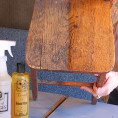 a person holding onto a wooden chair and cleaning it with a spray bottle on the table