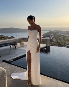 a woman standing on top of a roof next to a pool wearing a white dress