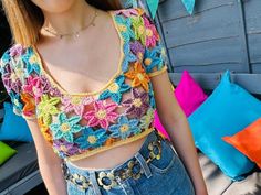 a woman wearing a colorful crochet top and jeans