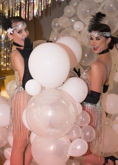 two women dressed in flappers and garb standing next to giant white balloons at a party