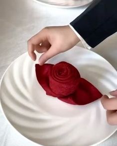 a person is decorating a white plate with red cloth on it and holding a rose in their hand