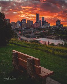 a wooden bench sitting on top of a lush green field next to a river under a cloudy sky