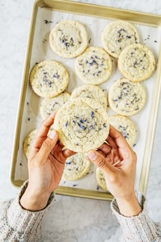 a person holding a cookie in front of some cookies on a baking sheet with blue and white sprinkles