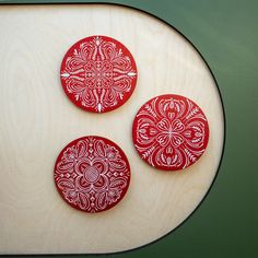 three red coasters sitting on top of a wooden table next to a green wall