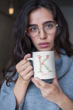 a woman wearing glasses holding a coffee mug with flowers on the front and side of it