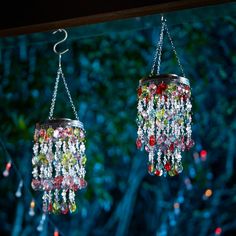 two tin cans filled with beads and chains hanging from the ceiling in front of trees