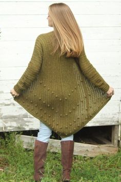 a woman standing in the grass with her back to the camera, wearing a green sweater and brown boots