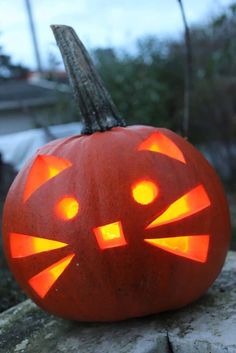 a carved pumpkin with glowing eyes and a cat's head on it, sitting on a rock