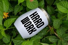 a white coffee mug with the word work on it sitting in some green leaves and flowers