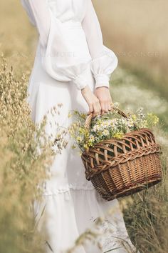 a woman in a white dress holding a wicker basket with daisies on it