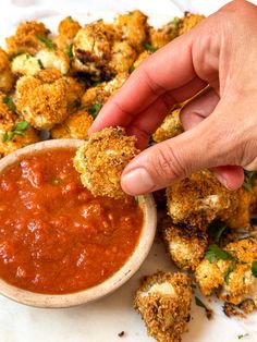 a person dipping something into a bowl of tomato sauce with fried cauliflower in the background