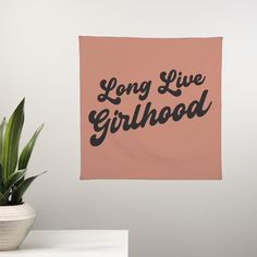 a pink wall hanging with the words long live girlhood on it next to a potted plant