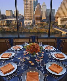 the table is set with plates, silverware and orange napkins