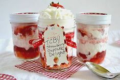 three jars filled with strawberry shortcake desserts on top of a red and white checkered table cloth