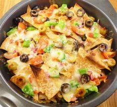 nachos in a skillet with cheese, olives, peppers and other toppings