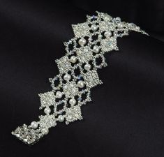 a close up view of a bracelet with pearls and crystals on black silk fabric,