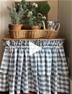 some plants are sitting on top of a table with a blue and white checkered skirt