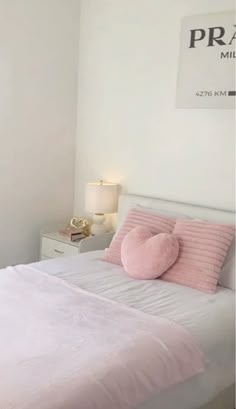 a white bed with pink pillows in a bedroom next to a wall mounted sign that reads pram mill