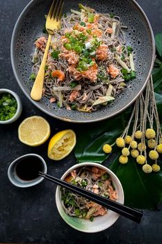 a bowl filled with noodles and vegetables on top of a table next to lemons