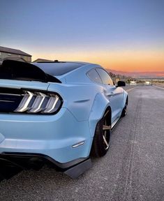 the rear end of a blue mustang car parked in front of a parking lot at sunset