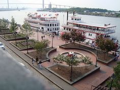 two large paddle boats docked next to each other on a riverbank with people walking around