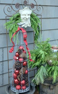 a metal basket filled with pine cones and red ornaments next to a potted plant