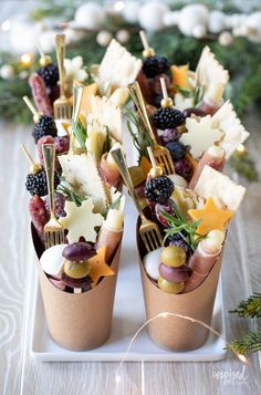 two cups filled with different types of appetizers on top of a table next to christmas decorations