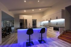 two bar stools sit in the middle of a kitchen with stairs leading up to it