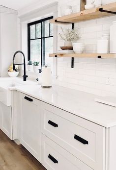 a white kitchen with open shelving and wooden shelves on the wall above the sink