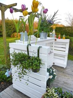 some flowers and plants are in white containers on a wooden deck near a garden area