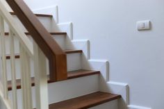 there is a light switch on the wall next to some white stairs with wood handrails