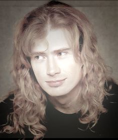 a man with long curly hair wearing a black shirt and looking at the camera while posing for a photo