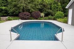 an empty swimming pool in the middle of a yard with trees and bushes behind it