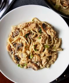 a white plate topped with pasta covered in mushrooms and sauce next to a skillet