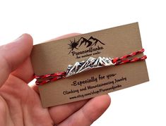 a person holding two red and silver bracelets with mountains on the back of them