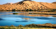 a lake surrounded by sand dunes in the middle of a desert area with blue water