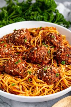 spaghetti with meatballs and parsley in a white bowl on a marble countertop