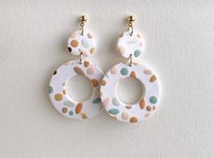 a pair of white and multicolored polka dot hoop earrings on a white background