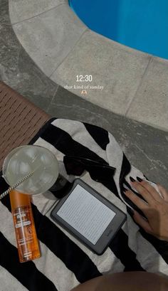 a woman sitting next to a swimming pool with an ipad and book on her lap