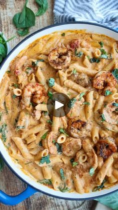 pasta with shrimp and spinach in a blue skillet on a wooden table next to basil leaves