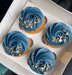 three cupcakes with blue frosting and sprinkles in a box