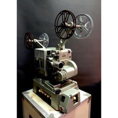 an old movie projector sitting on top of a wooden box in front of a black wall